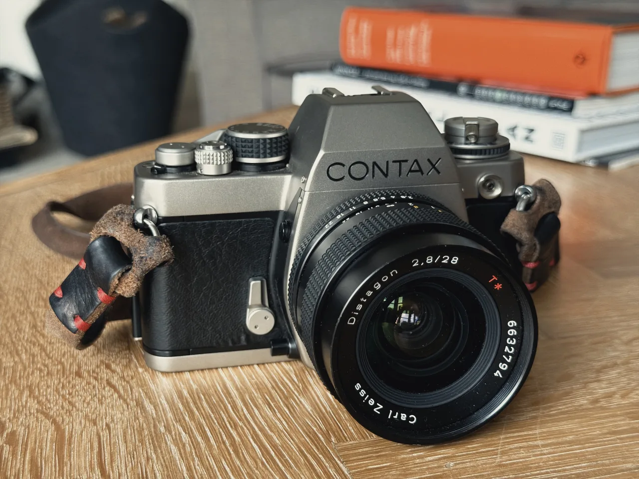 A titanium Contax S2 on a wooden table, fitted with a Zeiss Distagon 28mm f2.8 and a leather strap