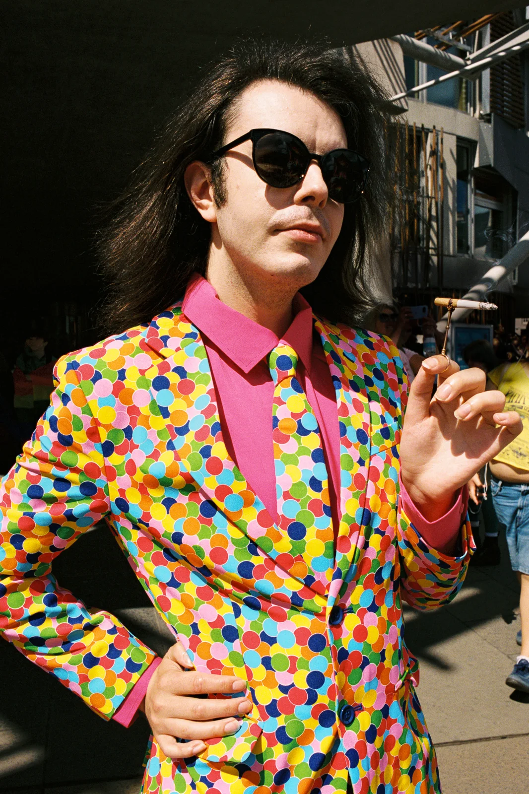 A man in sunglasses and a multicoloured polka dot suit holding a cigarette
