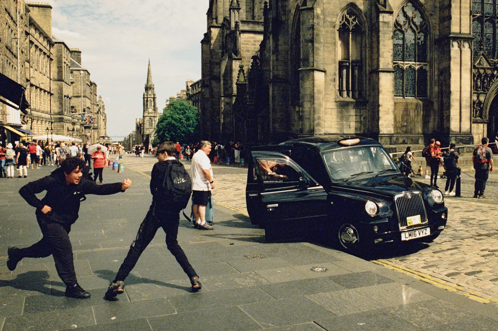Two teenagers mid-stride beside a black cab outside St Giles' Cathedral