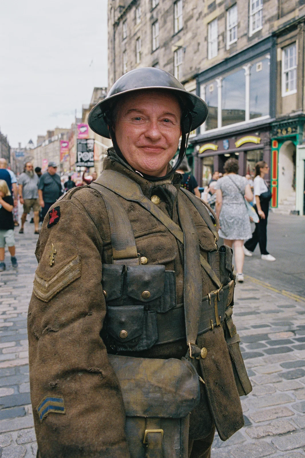 A man dressed as a First World War soldier in helmet and uniform, smiling on a busy cobbled street