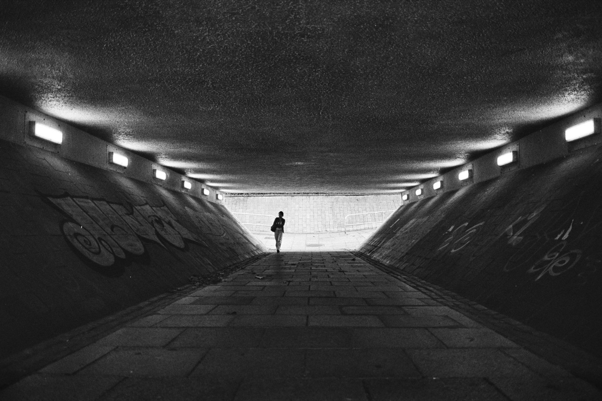 Lone figure at the end of a graffitied underpass